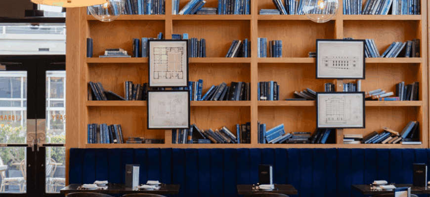 interior of a restaurant with a large bookcase on the wall and two blue chairs in front.