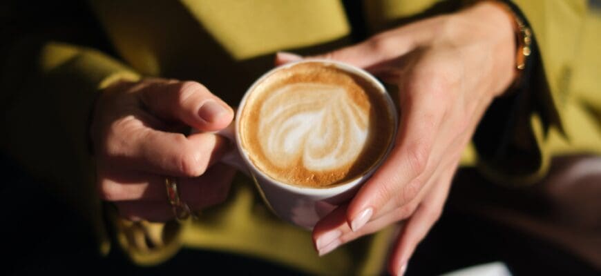 Close-up,Hands,Holding,A,Cup,Of,Coffee,Against,The,Background