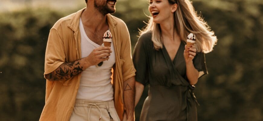 A man and woman smiling and walking together while holding ice cream cones